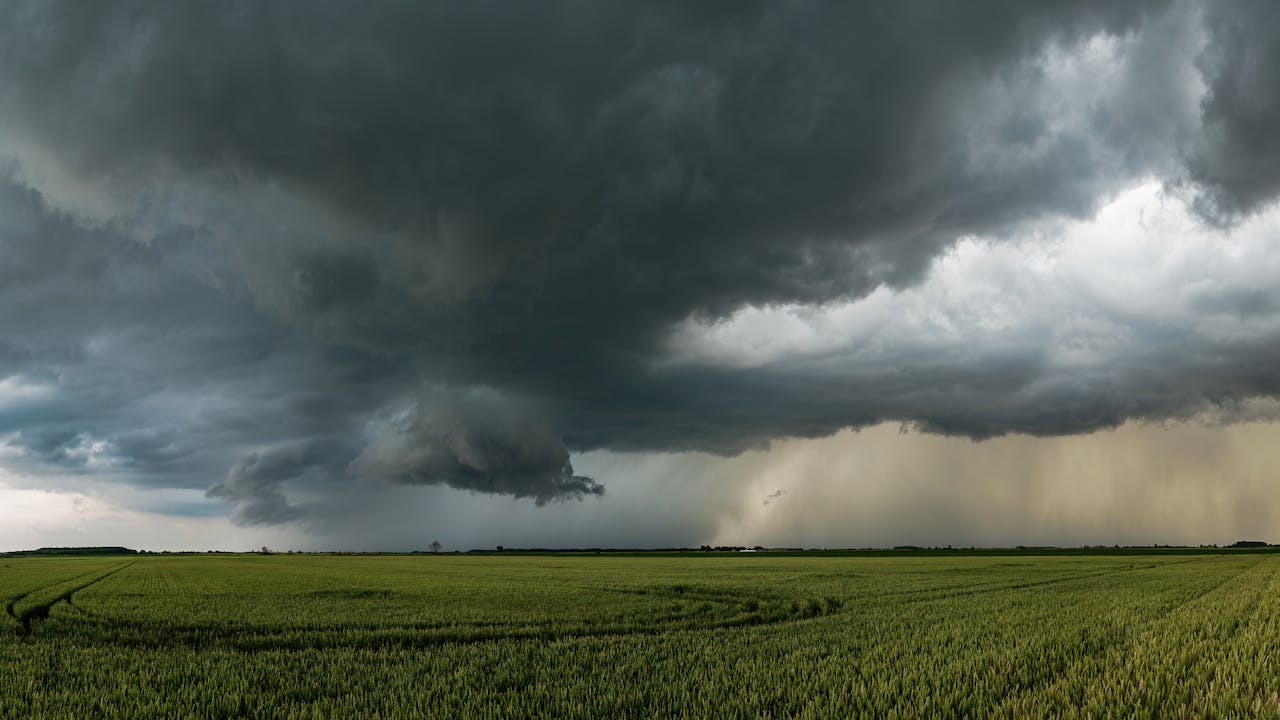 A panoramic shot of a vast green field under dramatic storm clouds, showcasing rural beauty.